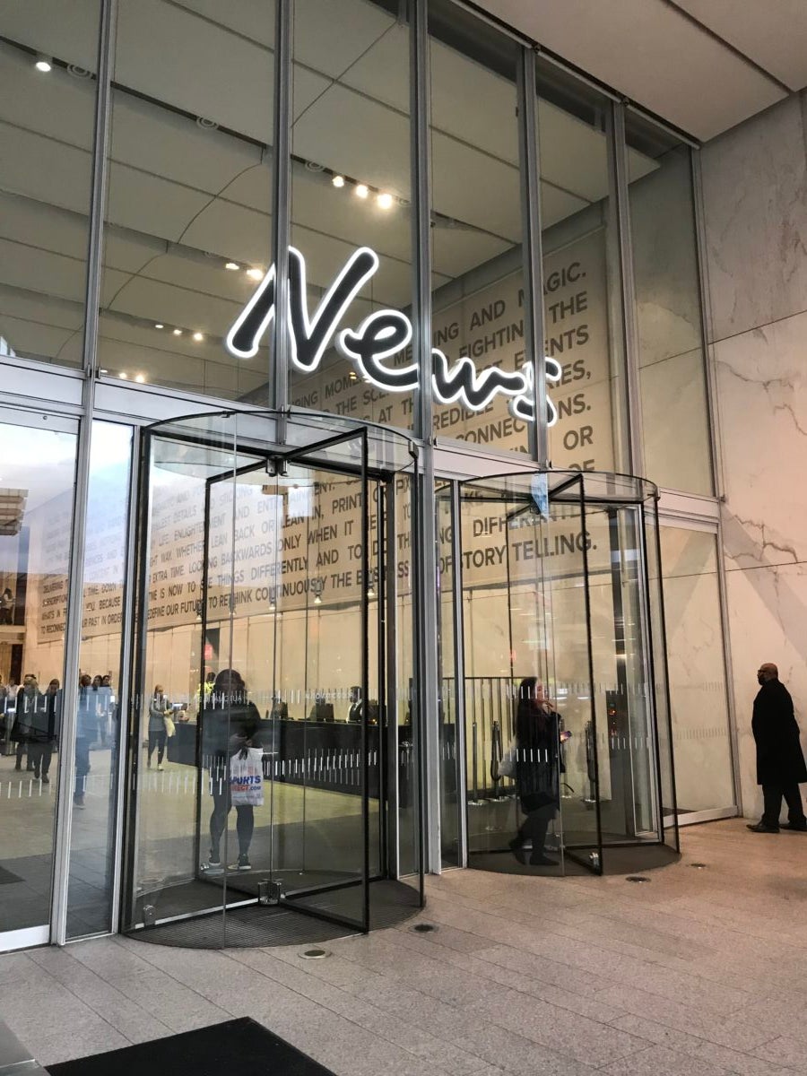 Entrance to News UK building with glass walls, revolving doors and a big sign saying 'News' over the doors