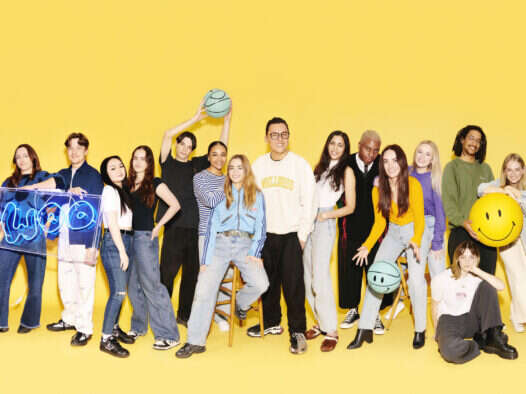 ITV Woo: Team shot of 15 (mostly in their 20s) people smiling and playing with bouncy balls and basketballs in front of a yellow backdrop