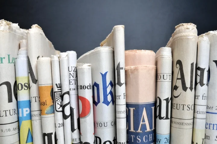Newspaper stack on a shelf against a dark blue wall