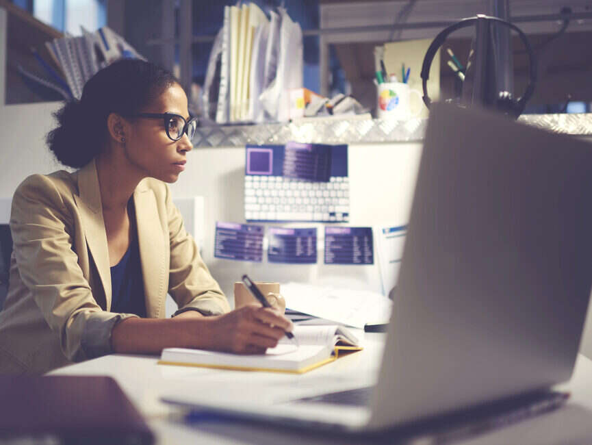 Woman at desktop with laptop and notebook