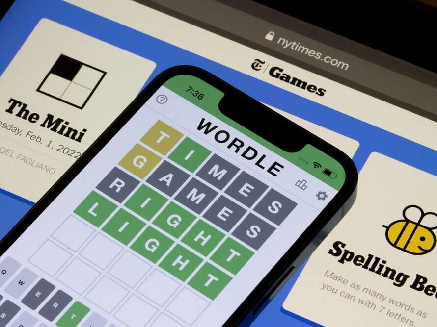 The New York Times' Wordle app is seen on a smartphone in front of The New York Times' Games section on a desktop browser