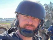 Ryan Evans looking at the camera outside dressed in a flak jacket and a helmet