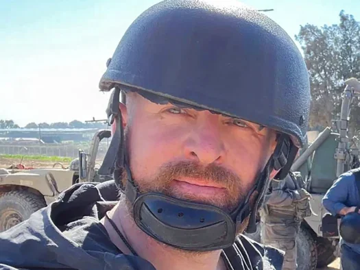 Ryan Evans looking at the camera outside dressed in a flak jacket and a helmet