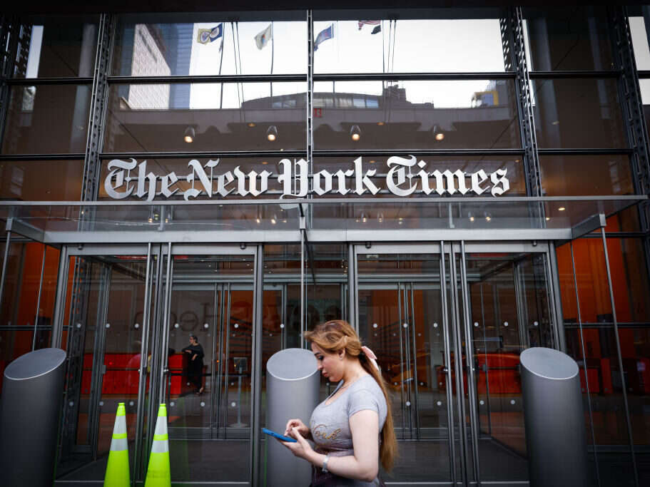 A person looking at their phone walks past The New York Times building, illustrating a story about The New York Times' revenue growth strategy built around 'bundles'.