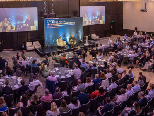 Press Gazette editor-in-chief Dominic Ponsford is seen from afar, on stage in a large room full of people, interviewing Future chief executive Jon Steinberg at the start of the 2023 Future of Media Technology Conference. Among other topics, they spoke about how the publisher is using generative AI at the moment.