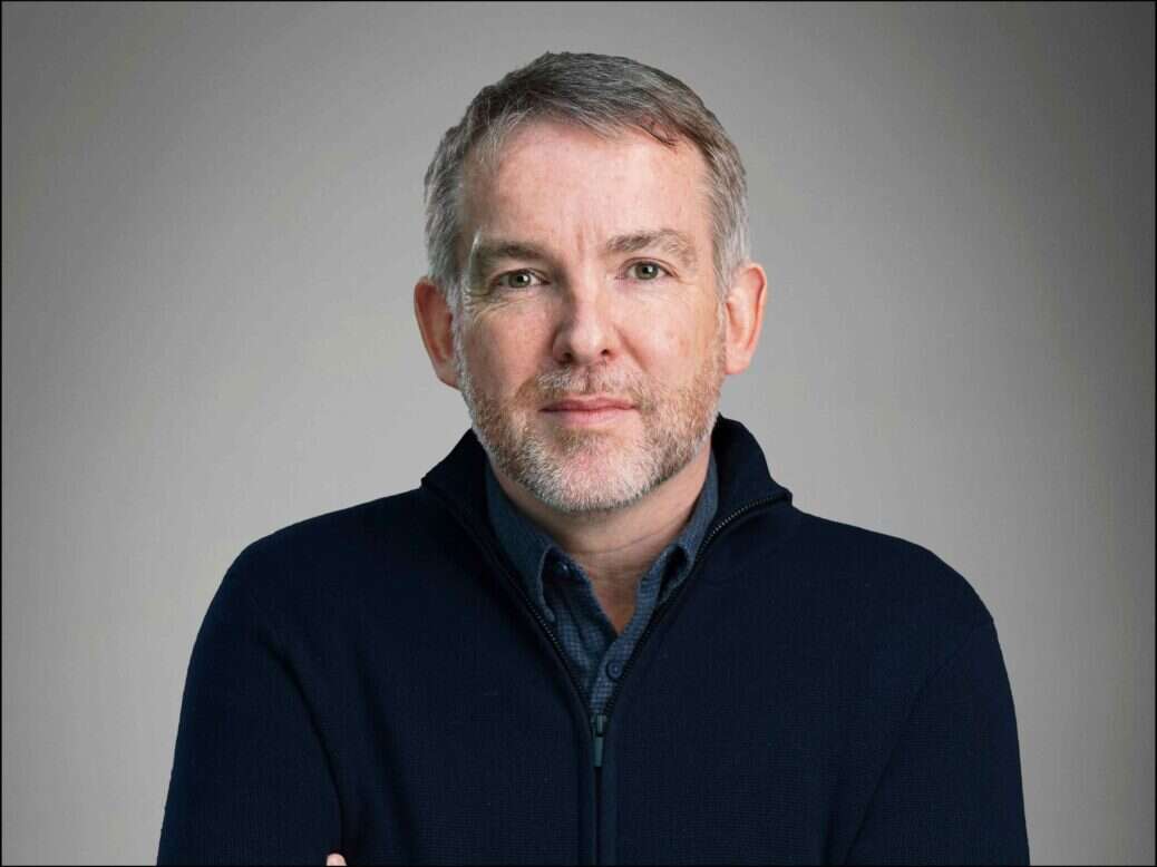 BBC Nations director Rhodri Talfan Davies is depicted in a quarterzip against a grey background.