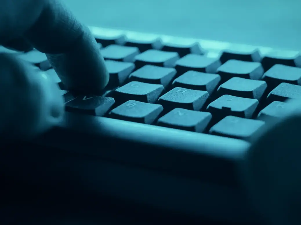 A close-up picture of fingers at a computer keyboard in moody blue colours, illustrating a story about how the news industry became a major target for cyberattacks/hackers.