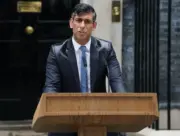 Rishi Sunak standing at a wooden lectern in front of the famous 10 Downing Street door with a rain-sodden suit on