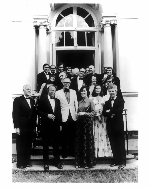 Black and white photo of about 20 people dressed in black tie standing on steps of a grand building