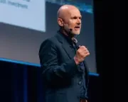 Mediahuis CEO Gert Ysebaert stands on stage dressed in a suit mid-presentation, in front of a huge slide projector