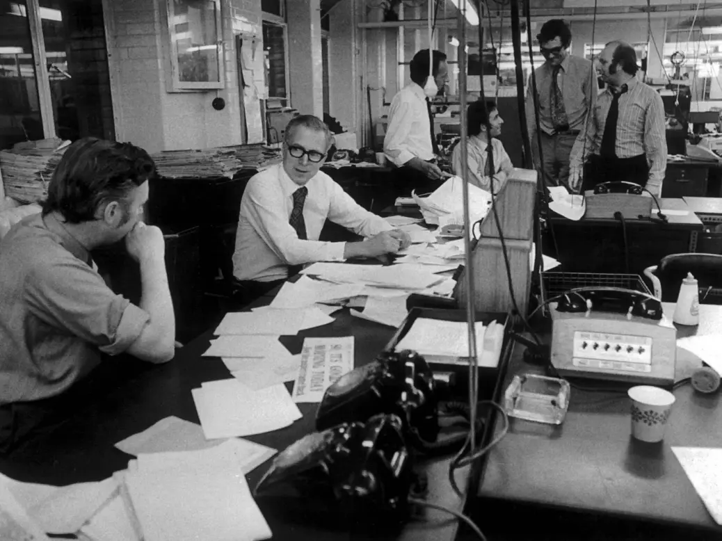 Evening Standard newsroom in the 1970s - black and white image showing six men in shirts and ties at desks covered in paper