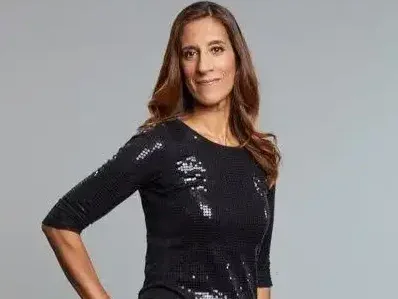 TBIJ CEO Rozina Breen stands smiling at the camera with one hand on her hip wearing a sparkly black top