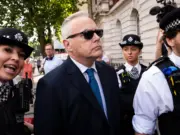 Former BBC broadcaster Huw Edwards arriving at Westminster Magistrates' Court wearing a suit and sunglasses and surrounded by several police officers