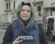 Emma Murphy dressed in flak jacket labelled 'press' and head covering, giving piece to camera