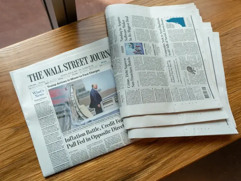 Two copies of Wall Street Journal print newspaper on a newspaper, one showing Trump charges story on top half of the front page and one showing the bottom half sideways-up