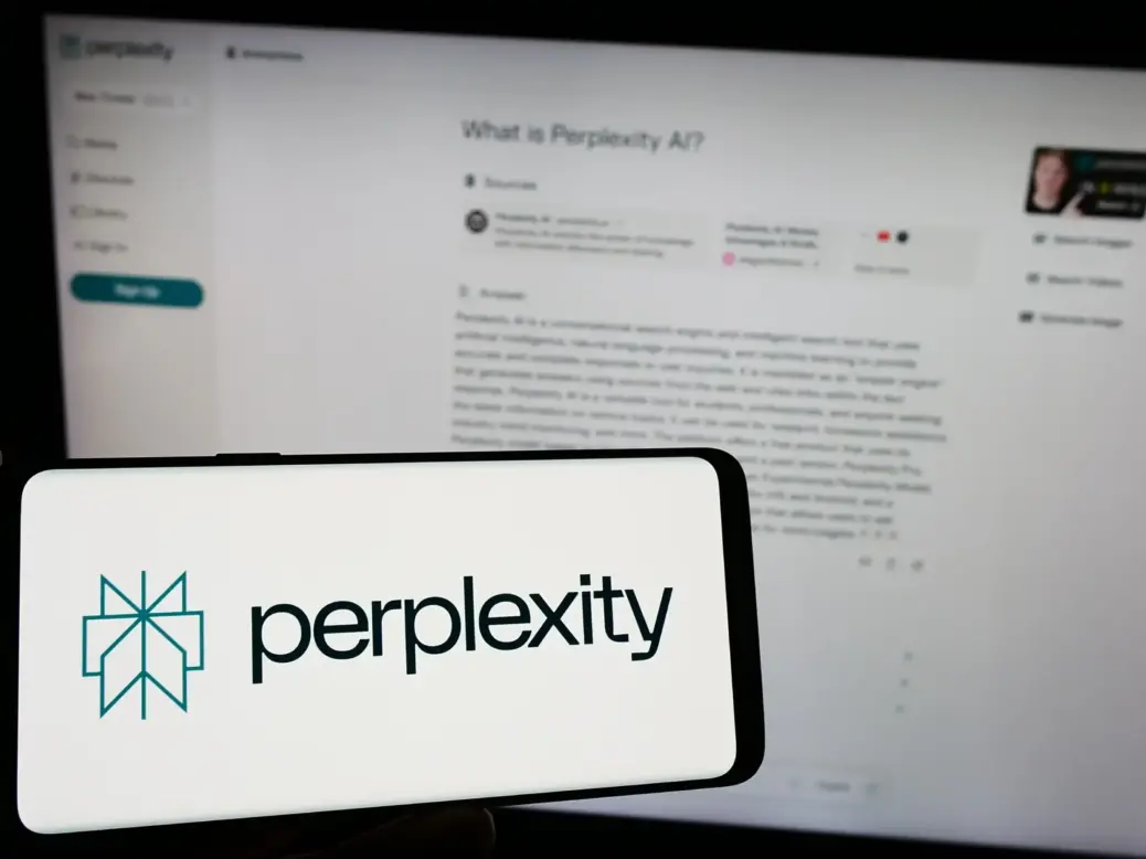 Perplexity logo on a phone in front of computer screen showing PerplexityAI chat in use