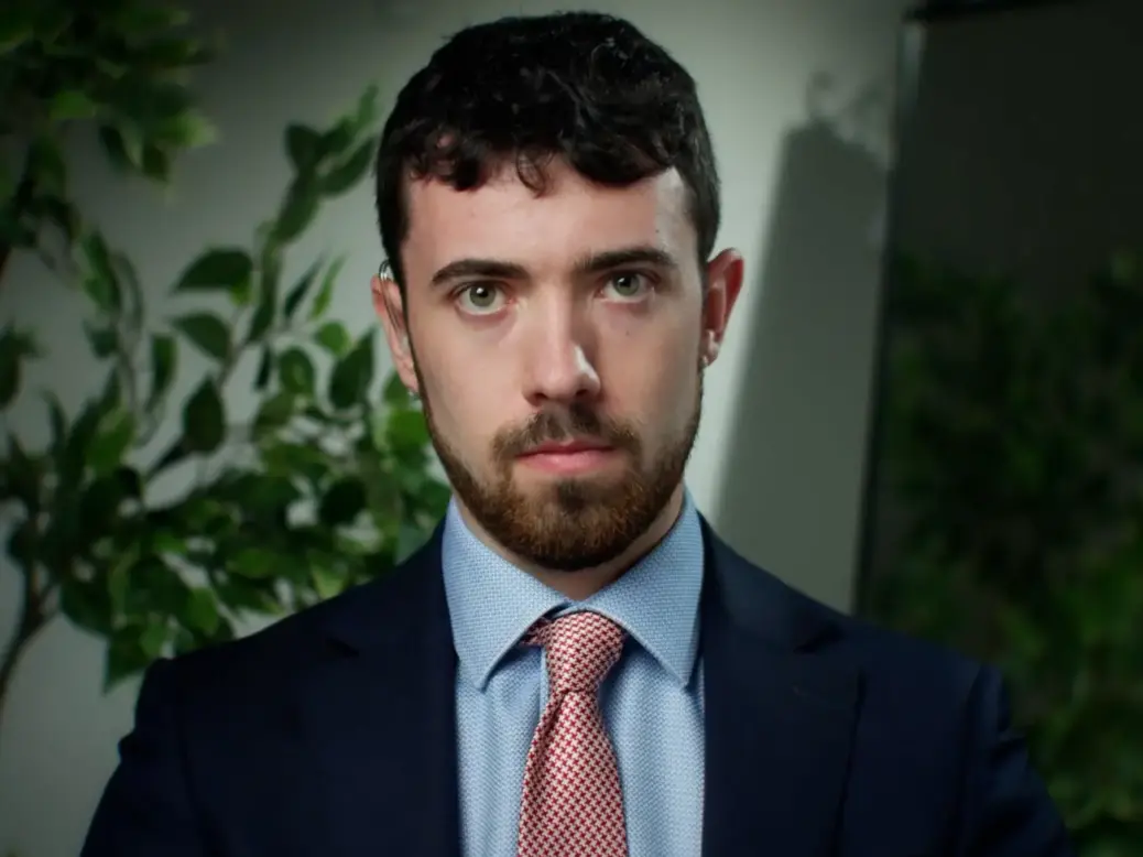 GB News US correspondent Steven Edginton looks straight at the camera dressed in a suit with a plant in the background