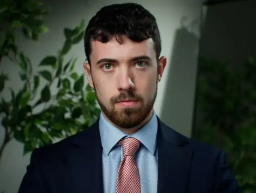 GB News US correspondent Steven Edginton looks straight at the camera dressed in a suit with a plant in the background