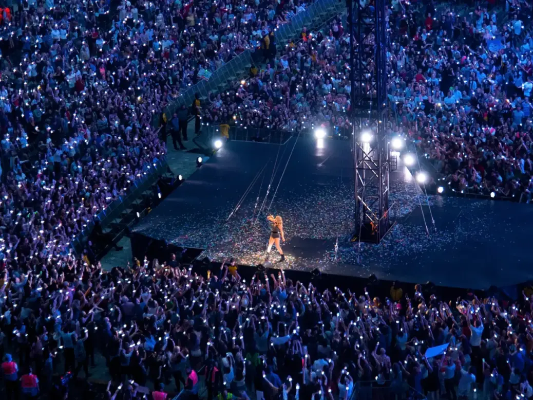 Taylor Swift on a stage in the middle of a stadium with crowd lit up all around her