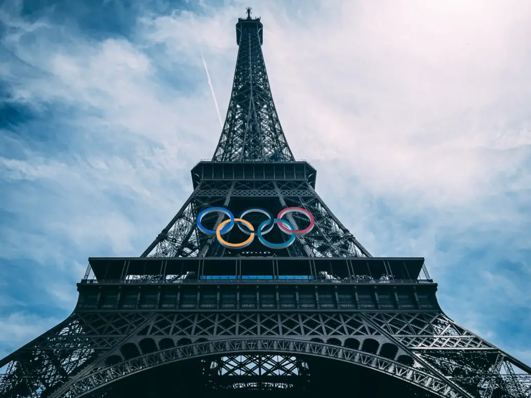 Shot from the ground looking up at the Eiffel Tower with the Olympic Rings installed in the centre. Blue sky behind it