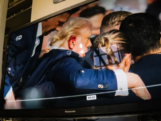 Picture shows TV with paused image of Donald Trump with a bleeding ear being escorted by Secret Service agents around him