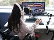 Woman sits at desk with headphones on, a microphone and a sound mixing programme on the monitor