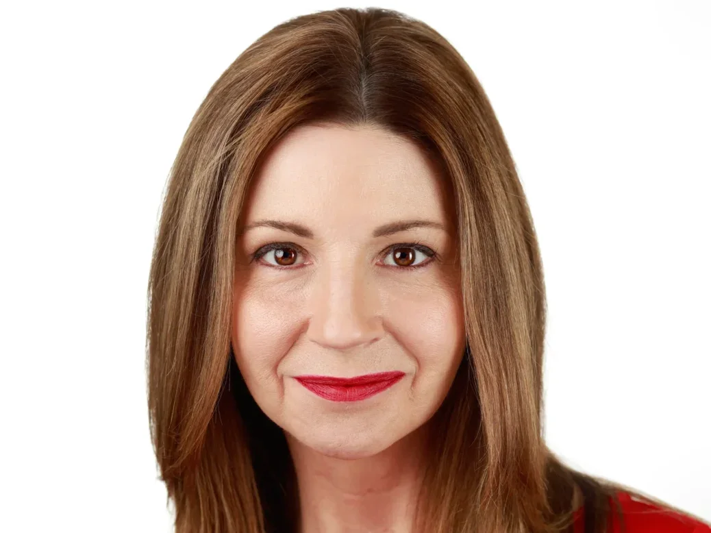 Traci Mabrey, general manager of Factiva. Traci is smiling at the camera and wearing a red top. There is a plain white backdrop behind her.