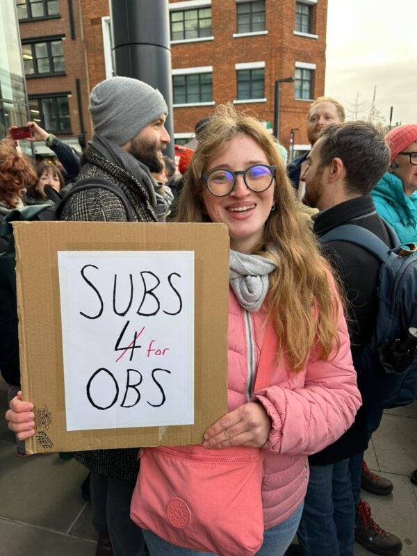 Woman on picket line holding placard saying 'subs for OBS'.