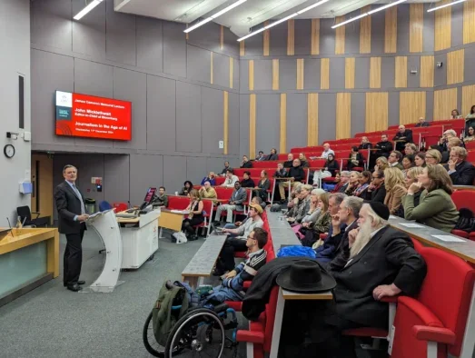 Bloomberg editor-in-chief John Micklethwait appears in front of a crowd in a lecture hall at City University, London, where he speaks about journalism business models, paywalls, the effects of AI and lawfare.