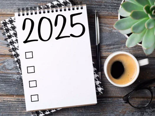 A paper pad on a wood tabletop has the year "2025" written across the top. It is next to a fresh mug Americano and a succulent.