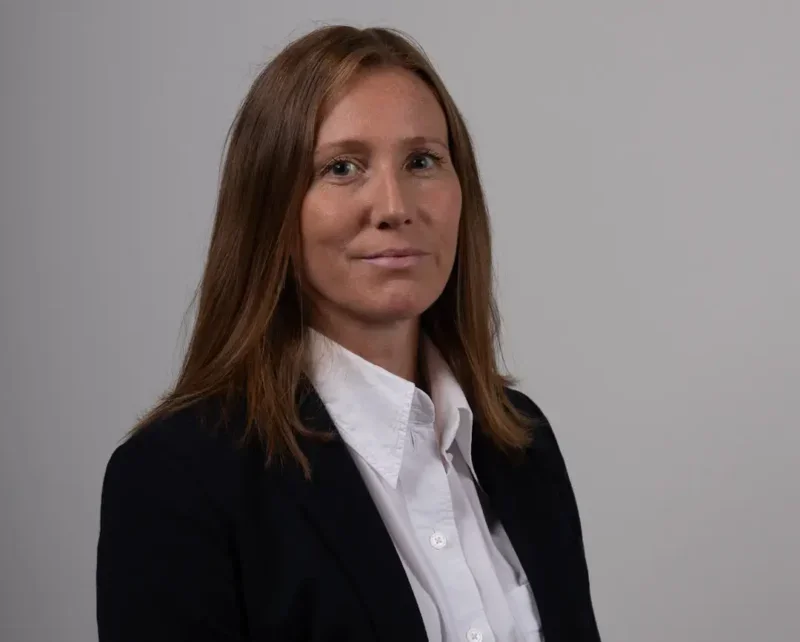 Chloe Hubbard headshot dressed in black blazer and white shirt with grey background