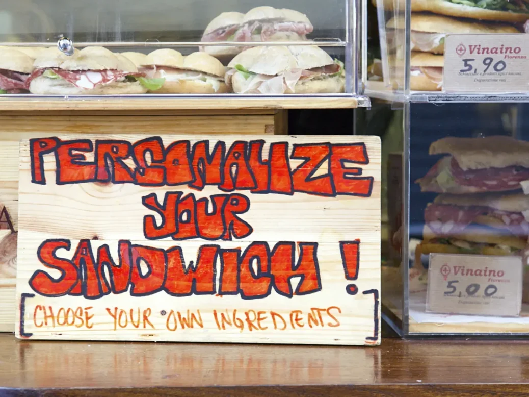 Sign propped up in front of sandwiches behind cafe counter says "Personalise your sandwich! Choose your own ingredients". Used to illustrate article about AI-powered personalisation.