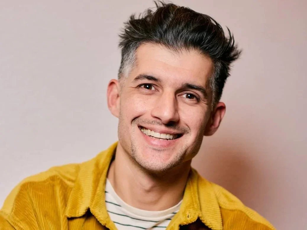 Laurence Mozafari smiling at camera wearing a yellow shirt with a plain backdrop