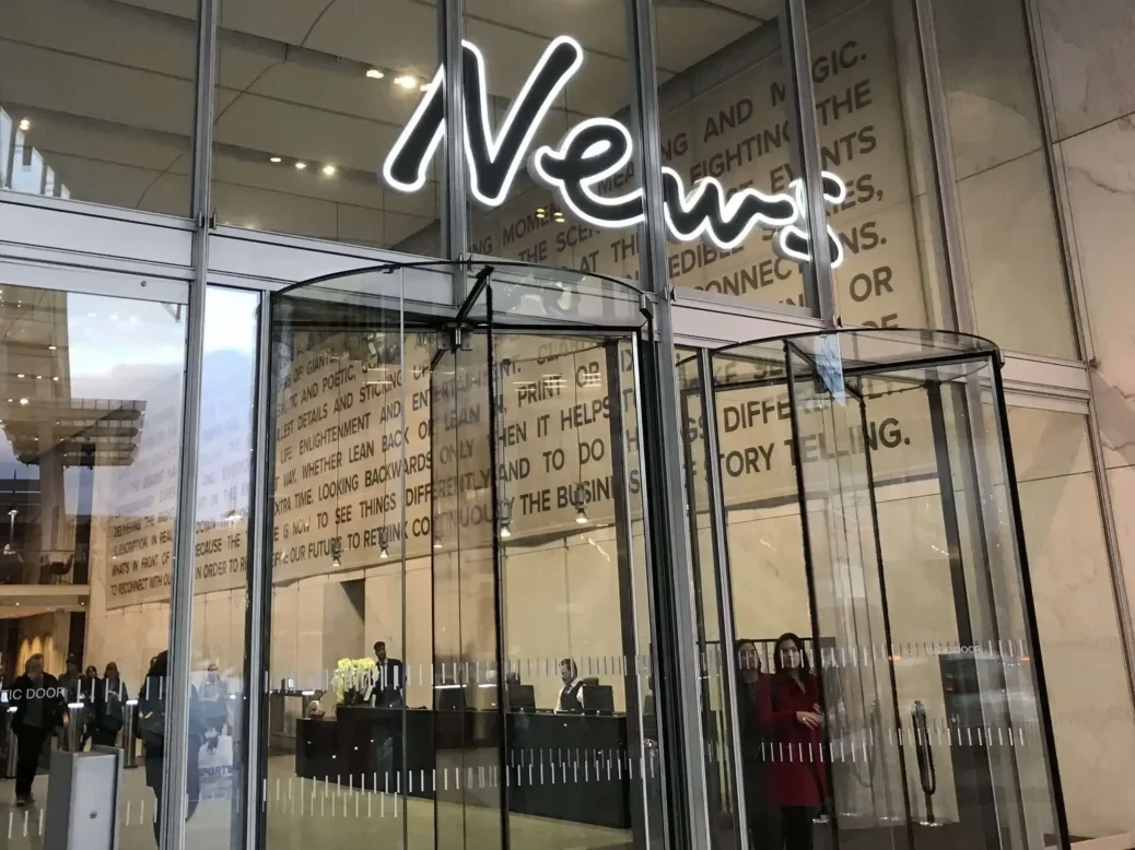 Entrance to News UK building with glass walls, revolving doors and a big sign saying 'News' over the doors