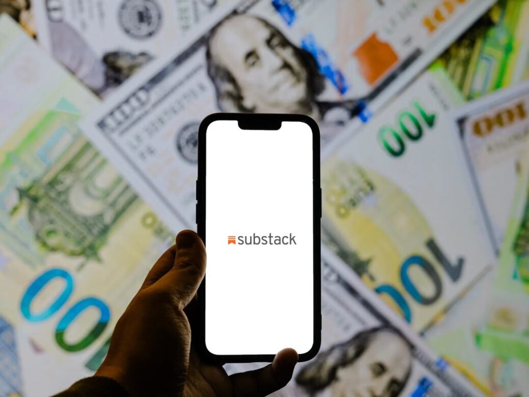 An iPhone with the Substack app is held in front of bills of money in various currencies, illustrating a Press Gazette article about the highest-earning Substacks.