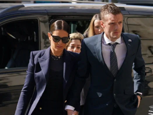 Rebekah and Jamie Vardy in smart clothes walking towards the camera with a car behind them