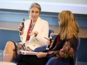 Associated Press chief revenue officer Kristin Heitmann discussing advertising trends and other hot topics, sitting down and holding a microphone while speaking and looking towards another woman whose back is to the camera