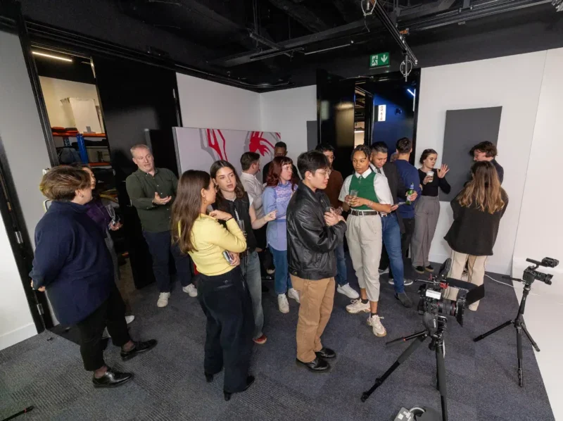 Staff standing up and talking in groups, some holding drinks, in video studio