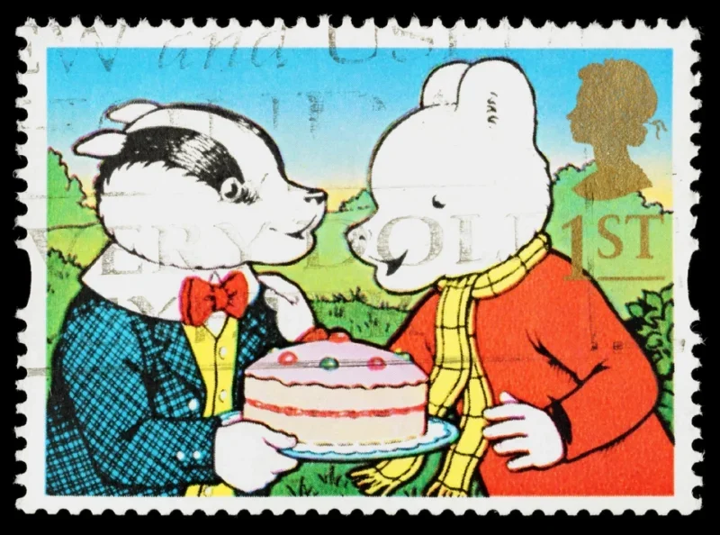 A used postage stamp printed in Britain showing Rupert Bear and Bill Badger holding a cake