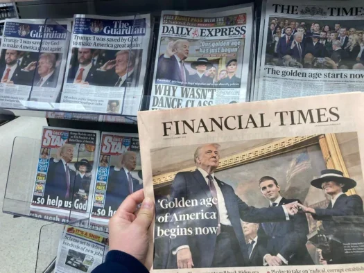 A UK newsstand displays newspapers the morning after Donald Trump's second inauguration in January 2025. The photographer holds a copy of the Financial Times up to the camera, which carries the headline "'Golden age of America begins now'" over a picture of Trump being inaugurated.