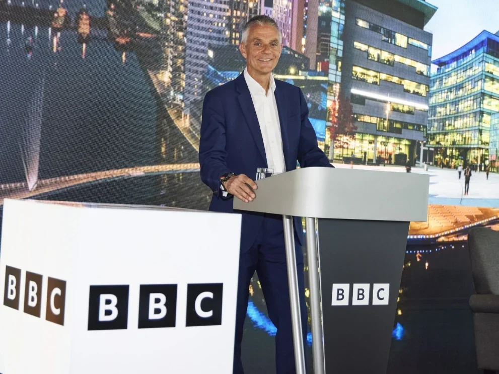 BBC director-general Tim Davie stands behind BBC-branded lectern next to BBC-branded stage furniture