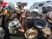 Young Palestinians crowded on a street waving kitchen pans towards the camera