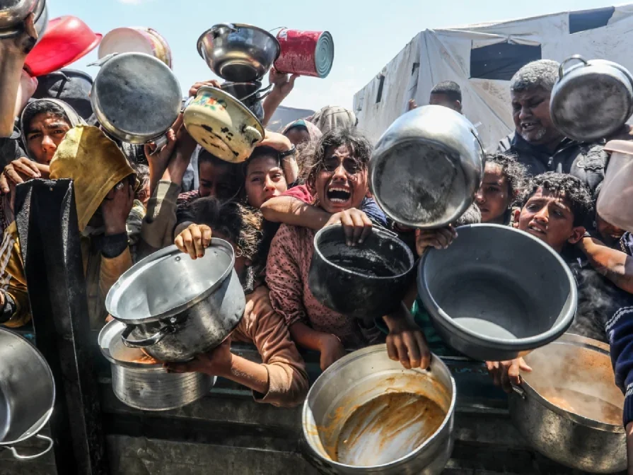 Young Palestinians crowded on a street waving kitchen pans towards the camera