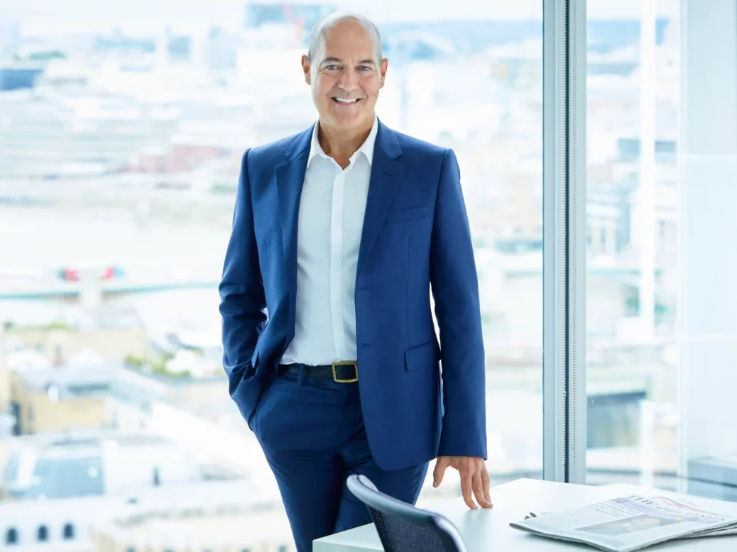Times Media head of digital Edward Roussel standing in front of a tall building's glass window, wearing a blue suit without a tie, smiling at the camera