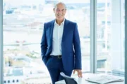 Times Media head of digital Edward Roussel standing in front of a tall building's glass window, wearing a blue suit without a tie, smiling at the camera