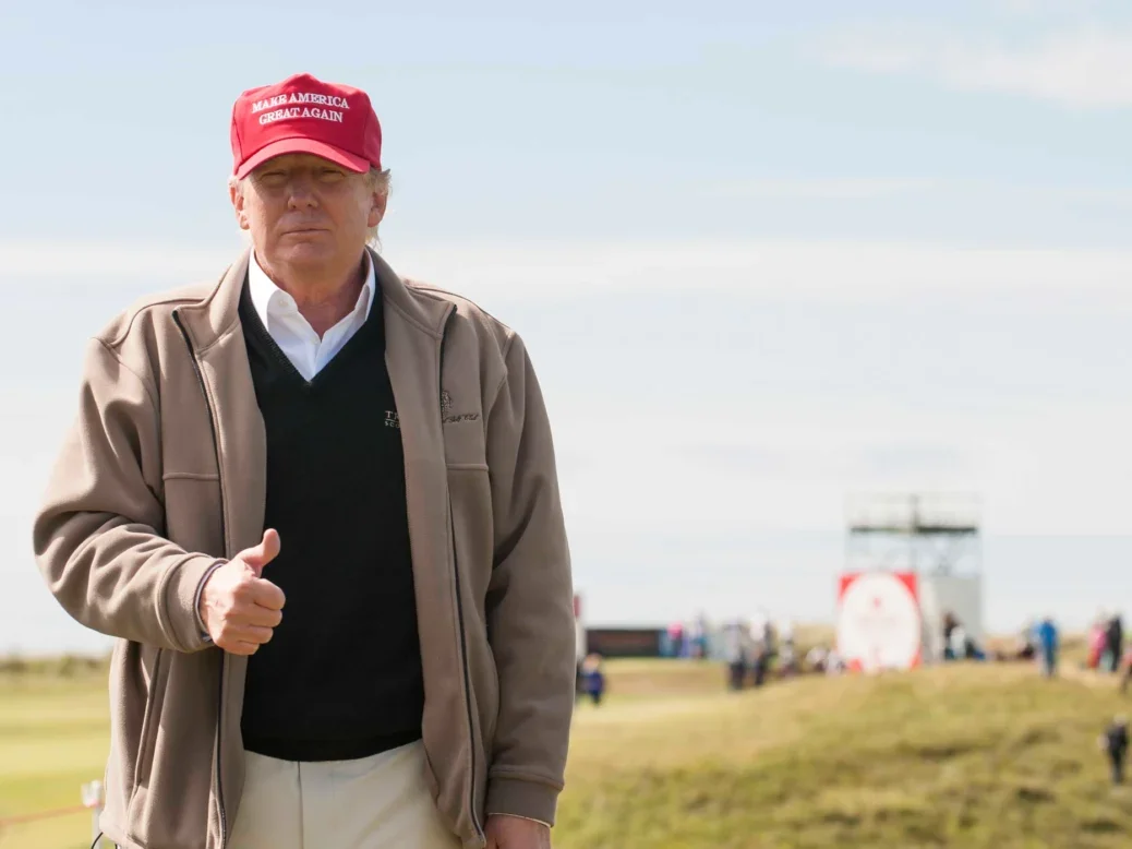 Donald Trump on a golf course wearing a Make America Great Again Hat doing a thumbs up gesture