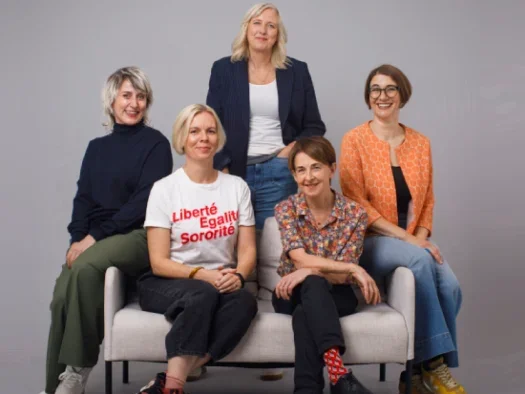 Founders of The Nerve, five women pictured sat on and standing around a sofa with a grey backdrop