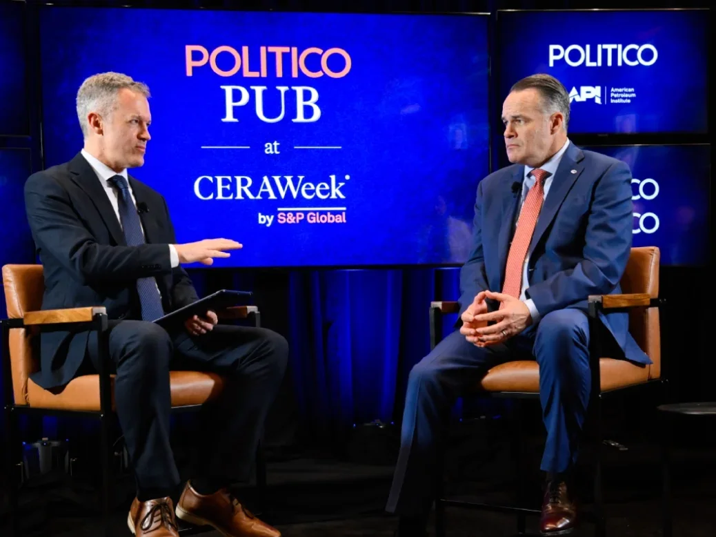 Politico deputy editor-in-chief Joe Schatz interviews American Petroleum Institute president Mike Sommers, both sitting on stools on stage, at the Politico Pub in CeraWeek with logos and branding behind them
