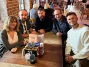 Helen Dalley, Luke Beardsworth, Mike Harris, Ed Walker and James Routledge of The Lead and The Knot around a large wooden table in a bar smiling at the camera