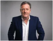 Piers Morgan in white suit, navy blazer and grey background